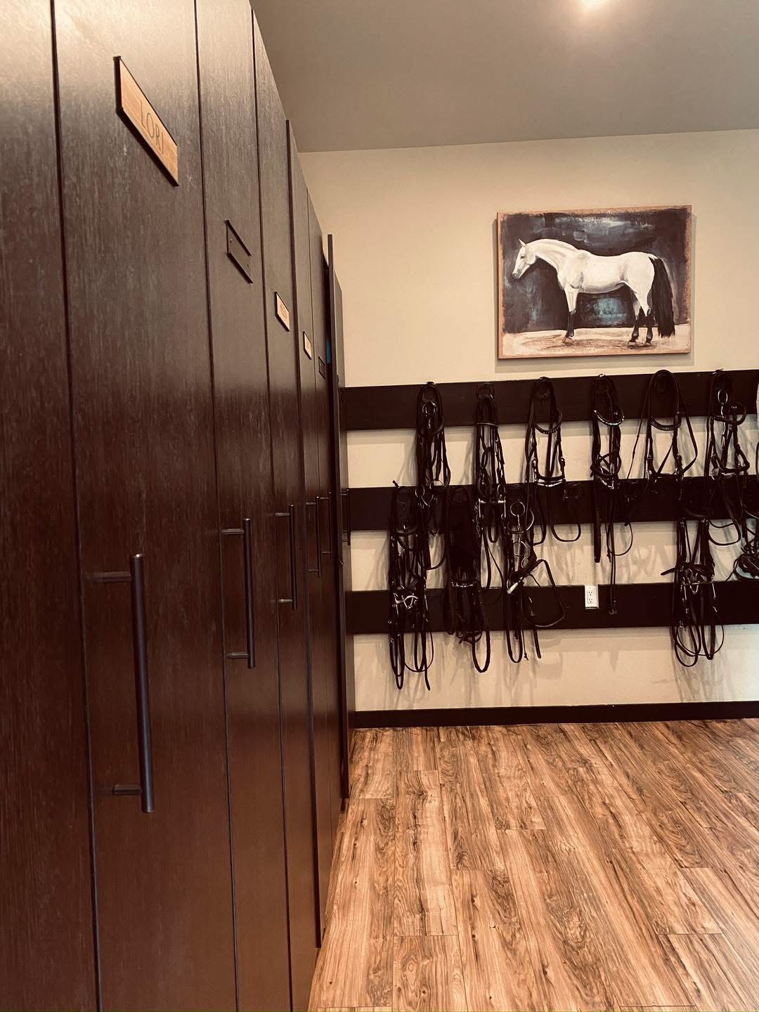 Custom tack room with dark wood lockers, bridle racks, and hardwood flooring